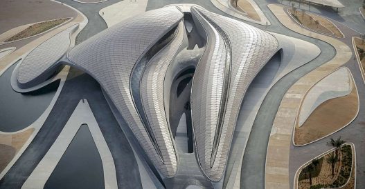 Luftaufnahme eines modernen, skulpturalen Gebäudes mit fließenden Linien und einem Metalldach.